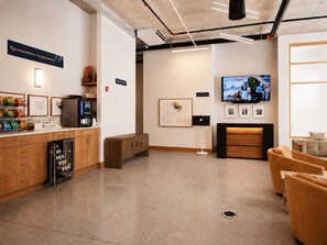 Una moderna estación de servicio con una máquina de café, zona de estar y un televisor que muestra un paisaje urbano.
