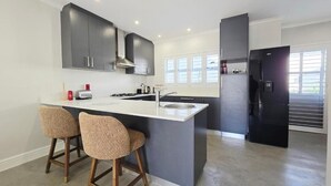 Een moderne keuken met donkere kastjes, een wit aanrecht en twee barkrukken.
