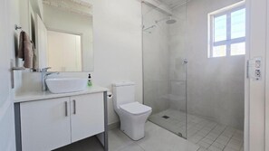Et moderne badeværelse med hvid vask, toilet og brusebad.