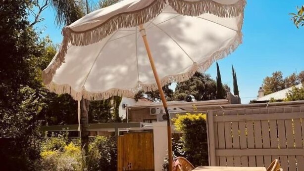 Een terras buiten met een tafel, stoelen, een witte parasol en een zwembad.