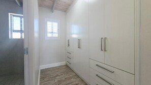 A hallway with a wooden floor, a window with blinds, and a white wardrobe with silver handles.