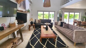 Ein geräumiges Wohnzimmer mit einem Flachbildfernseher, einer Couch, einem Couchtisch und einem großen Fenster mit Blick auf Grünflächen.