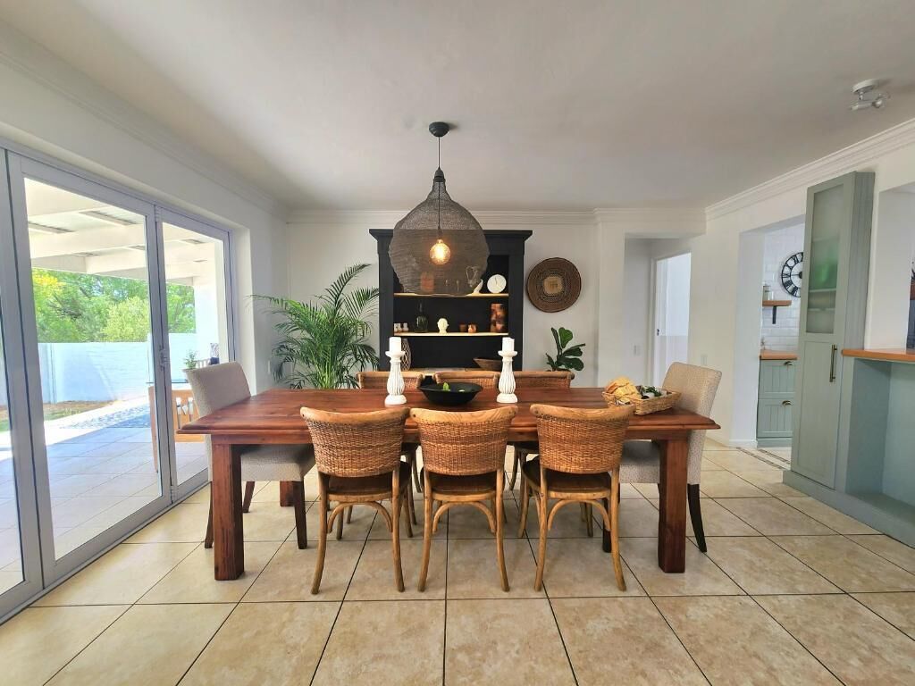 Un coin repas avec une table en bois, des chaises en osier, un luminaire suspendu et une vue à travers une porte vitrée.
