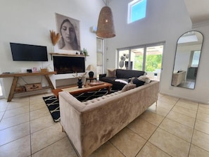 Una sala moderna con un sofá grande, un televisor de pantalla plana, una chimenea y un espejo amplio.