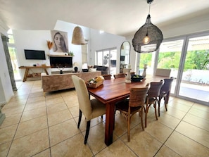 Amplia sala de estar con una mesa de comedor de madera, sillas de mimbre, un espejo grande y un televisor.