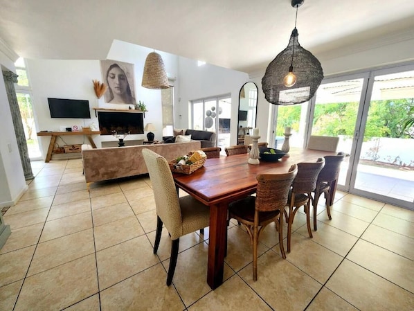 A spacious living area with a wooden dining table, wicker chairs, a large mirror, and a television.