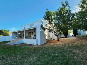 A modern house with a covered porch, a front yard with a tree, and a clear blue sky.