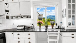Une cuisine avec des meubles blancs, un plan de travail noir et une fenêtre donnant sur les montagnes.