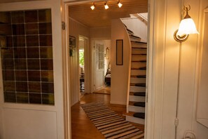 Un escalier avec un luminaire fixé au mur, un tapis à rayures sur le sol et une porte dotée d’une fenêtre en verre dépoli.
