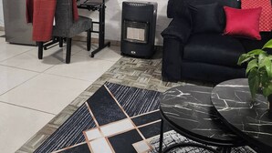 A living room with a sofa, a table, a heater, a refrigerator, and a mirror on the wall.
