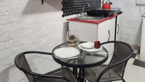 A compact kitchen with a red countertop, a sink, and a small dining area with two chairs and a glass table.