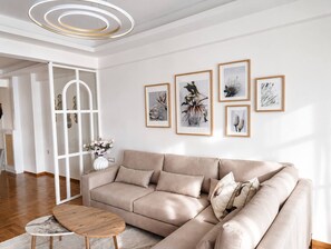 Ein modernes Wohnzimmer mit einem beigefarbenen Ecksofa, einem Holztisch und einem weißen Boden.