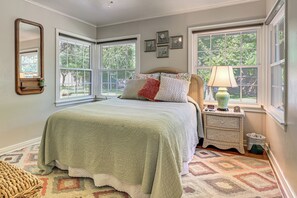 A bedroom with a bed, a nightstand, a lamp, a mirror, and two windows. - Walk to Shops & Eats! Family Escape in Columbus (Columbus)