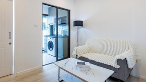 Een moderne woonkamer met een bank, een salontafel en een wasmachine zichtbaar door een glazen deur.