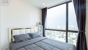 Een moderne hotelkamer met een groot bed, een hoofdeinde met gouden accenten, een nachtkastje en een uitzicht op de stad door grote ramen.