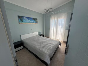 Ein Schlafzimmer mit einem Bett, einem Nachttisch, einem Gemälde und einem Fenster mit Vorhängen.