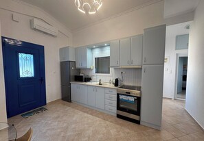 Eine kleine Küche mit grauen Schränken, einer blauen Tür, einem eingebauten Backofen und einer Mikrowelle.