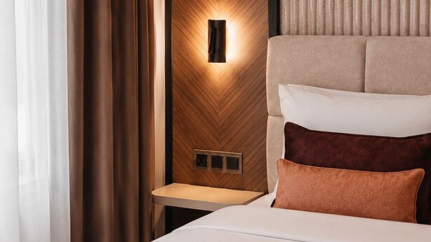 A hotel room with a bed, a nightstand, a wall-mounted light, and a window with curtains. - Nevv City Hotel (İstanbul)