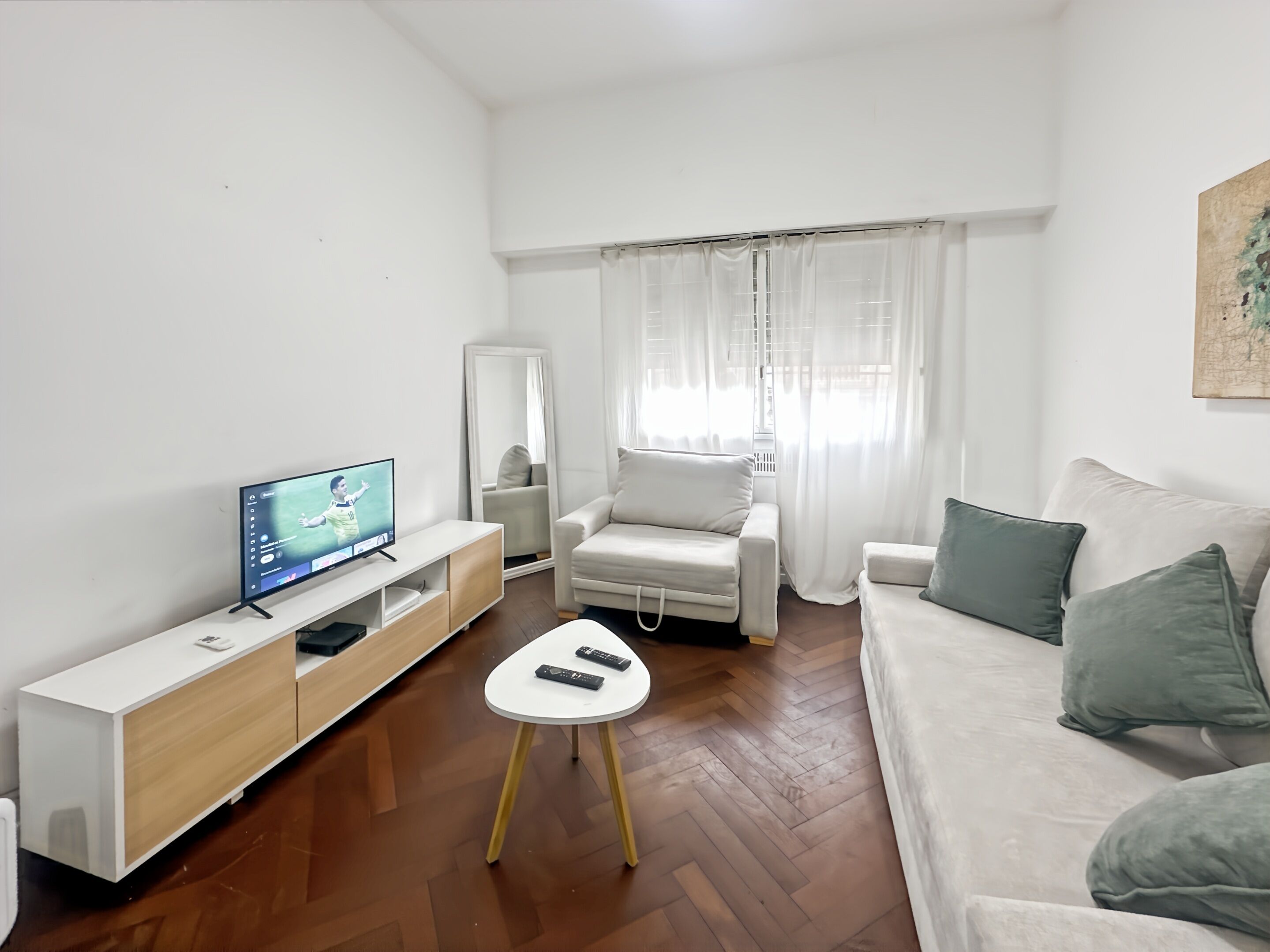 A living room with a TV, a white sofa, a chair, and a small table.