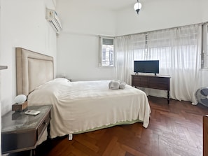 Quarto de hotel com cama, mesa de cabeceira, televisão e ventoinha.