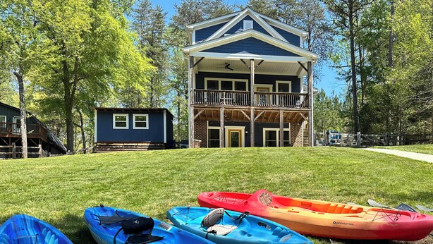 A two-story building with a balcony, surrounded by trees and a grassy lawn. - Lakehouse Blue: Fire Pit, Hot Tub on Lake Norman! (Sherrills Ford)
