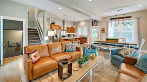 A spacious living area with a sofa, coffee table, and a dining table. A kitchen and staircase are visible in the background. - Lakehouse Blue: Fire Pit, Hot Tub on Lake Norman! (Sherrills Ford)
