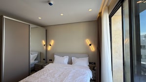 A hotel room with a large bed, bedside lamps, a mirror, and a view of the city. - 402 tara-JRE Jabal Al Lweibdeh with stunning view (Amman)