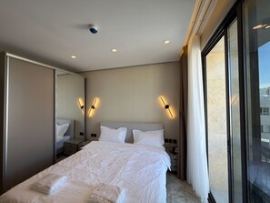 A hotel room with a large bed, bedside lamps, a mirror, and a view of the city. - 402 tara-JRE Jabal Al Lweibdeh with stunning view (Amman)