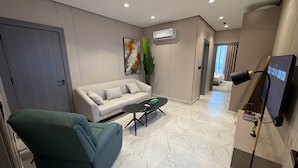 A modern living room with a sofa, a green armchair, a coffee table, a TV, and an air conditioning unit. - 402 tara-JRE Jabal Al Lweibdeh with stunning view (Amman)