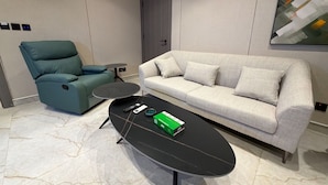 A modern living room with a teal recliner, a grey sofa, a black coffee table, and a small round table. - 402 tara-JRE Jabal Al Lweibdeh with stunning view (Amman)