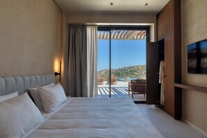 Een hotelkamer met een bed, een televisie, een balkon met stoelen en uitzicht op een glooiend landschap.