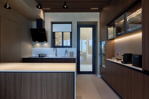 A modern kitchen with a central island, built-in appliances, and a view through a glass door. - Elysium Caved Salvia - Carved From Calm by etouri (Heraklion)