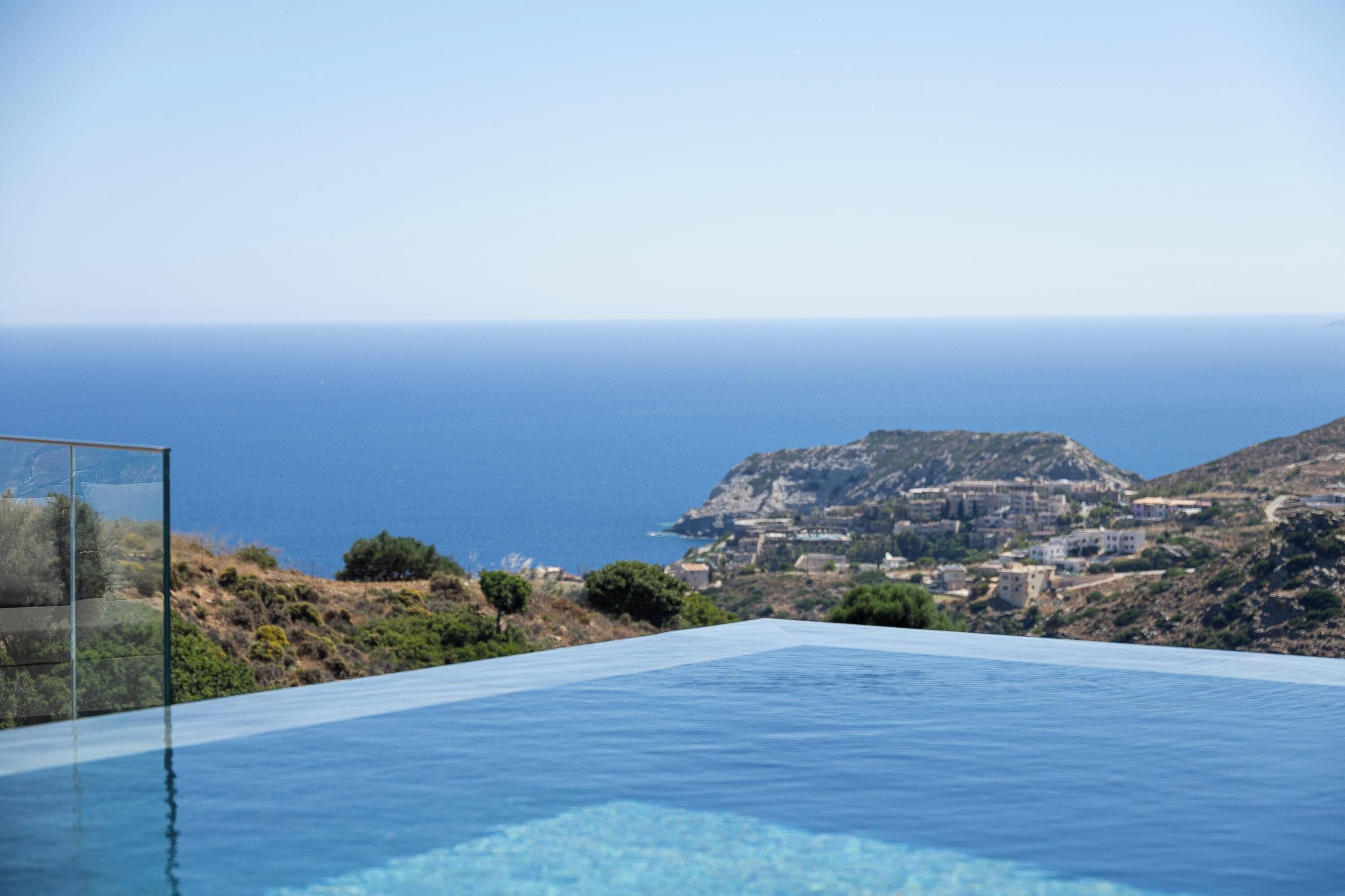 Uma piscina infinita azul e límpida com vista para o mar e uma cidade ao longe.