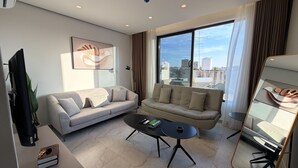 Een moderne woonkamer met twee banken, een salontafel, een televisie en een groot raam met uitzicht op de stad.