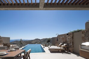 A poolside area with a view of the sea, outdoor furniture, and a stone wall. - Elysium Caved Majorana - Carved From Calm by etouri (Heraklion)