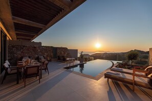 A sunset view from a modern outdoor dining area with a pool, stone wall, and wooden pergola. - Elysium Caved Majorana - Carved From Calm by etouri (Heraklion)