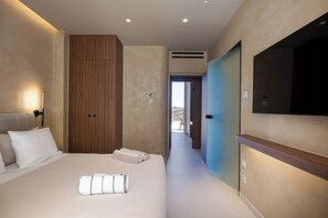A hotel room with a bed, a wooden wardrobe, a TV, and a view through an open door. - Elysium Caved Majorana - Carved From Calm by etouri (Heraklion)