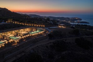 A modern resort with a swimming pool, outdoor seating, and a view of the sea at sunset. - Elysium Caved Majorana - Carved From Calm by etouri (Heraklion)