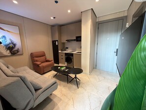Un espacio habitable compacto con sofá, sillón, mesa de centro, lavadora y zona de cocina.