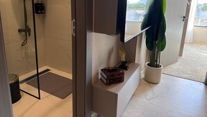 Ein modernes Badezimmer mit Duschkabine aus Glas, einem Waschtisch mit Spiegel, einer Zimmerpflanze und einem kleinen Regal mit Büchern.