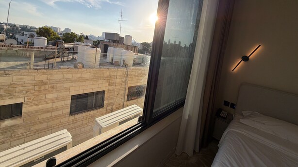 Ein Hotelzimmer mit großem Fenster, einem Bett, einem Nachttisch und einer Wandleuchte.