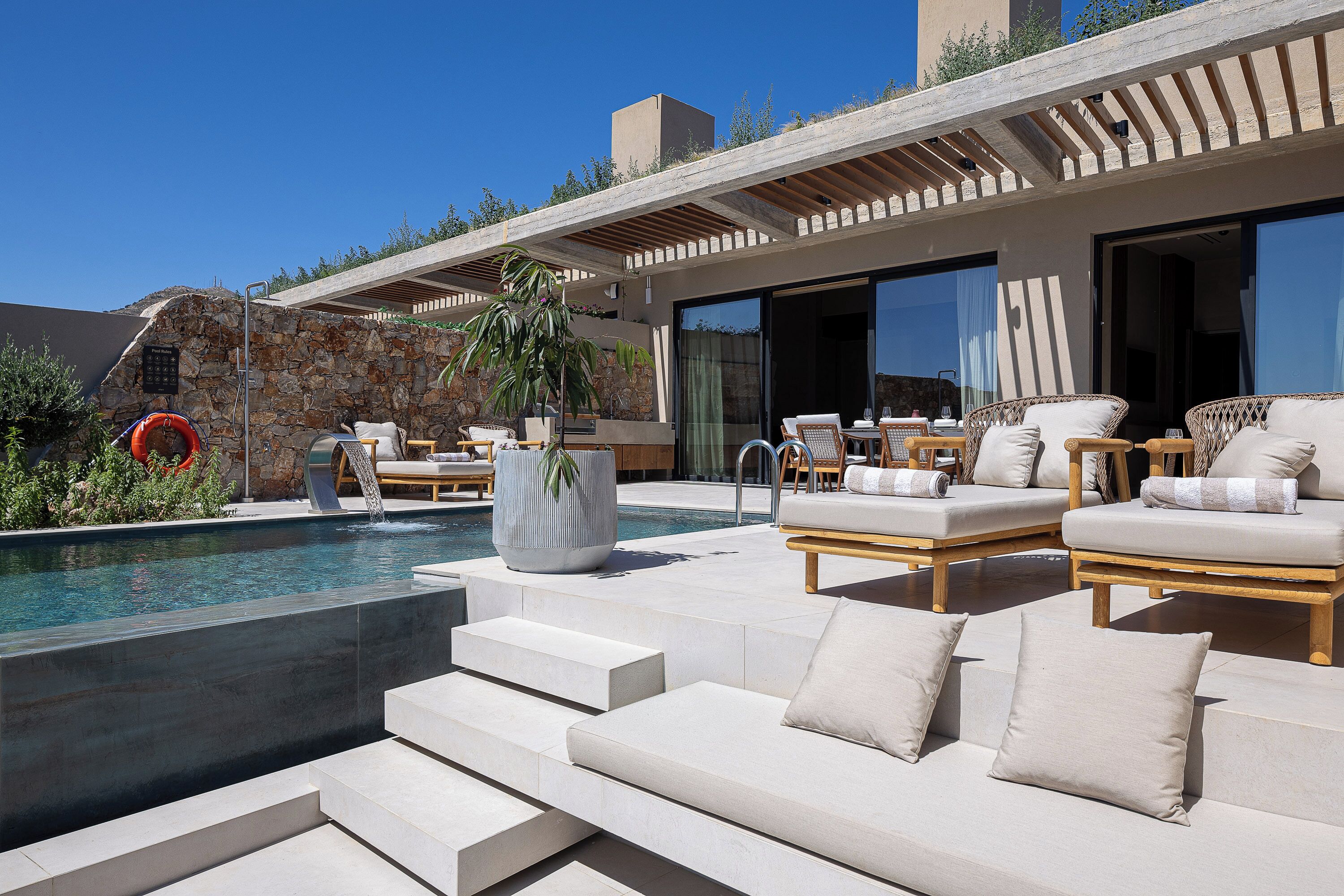 A modern outdoor pool area with tiered seating, lounge chairs, and a stone wall.