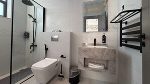 Ein modernes Badezimmer mit einer Duschkabine aus Glas, einer Toilette, einem Waschbecken mit Marmorplatte und einem Spiegel mit dekorativem Rahmen.