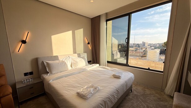 Ein Hotelzimmer mit einem großen Bett, einem Nachttisch, einem Sessel und einem Fenster mit Blick auf die Stadt.