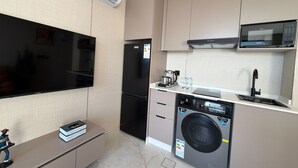 Eine kompakte Küche mit Einbau-Mikrowelle, Kühlschrank, Waschmaschine und Flachbildfernseher.