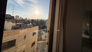 Aussicht aus einem Fenster auf eine Stadtlandschaft mit Gebäuden, einem klaren Himmel und einem Sonnenaufgang oder -untergang.