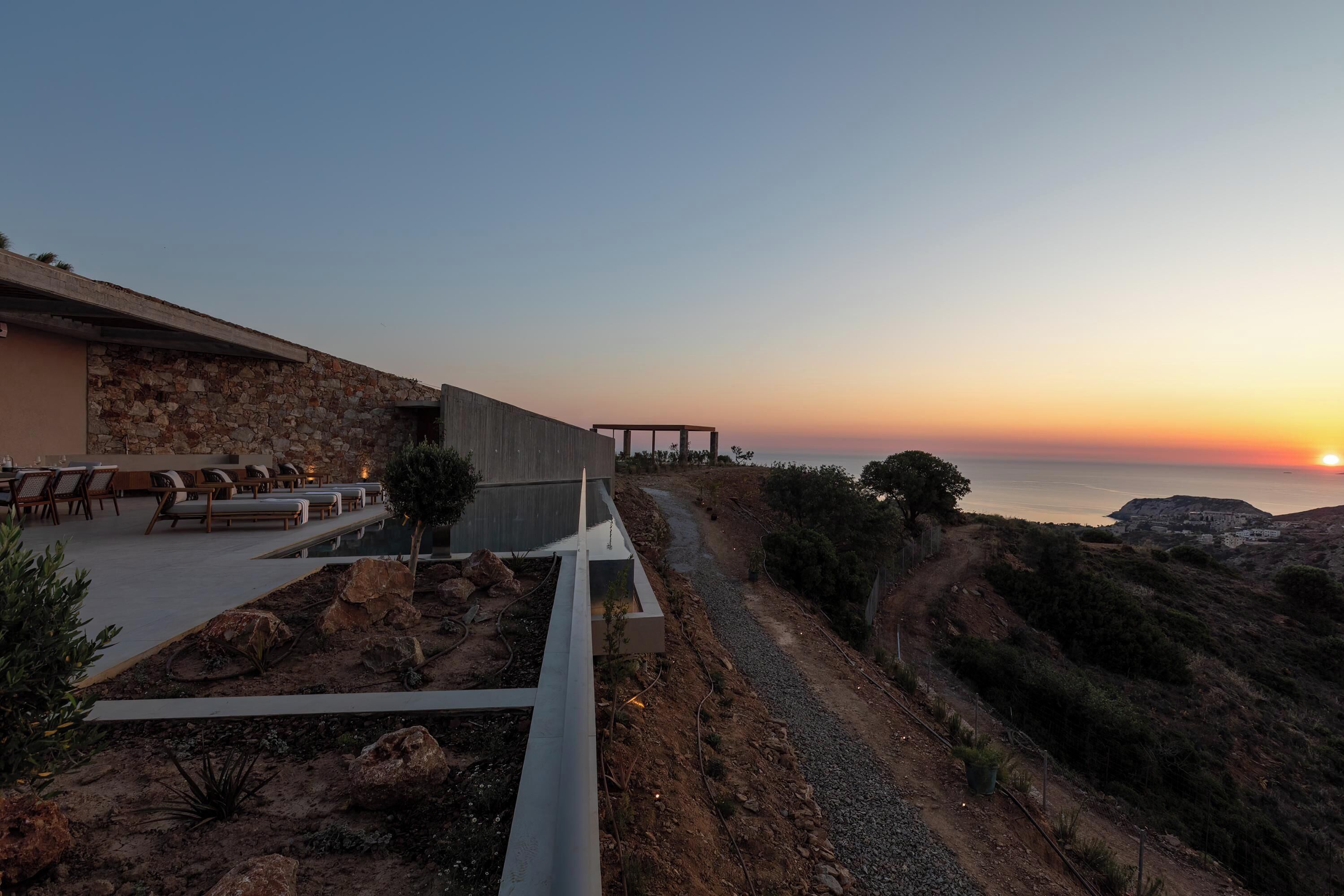 Hotel à beira-mar com área de estar externa, piscina e vista para o pôr do sol sobre o oceano.