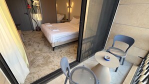 Habitación de hotel con cama, una pequeña mesa con sillas, un espejo y una puerta con perchero para toallas.