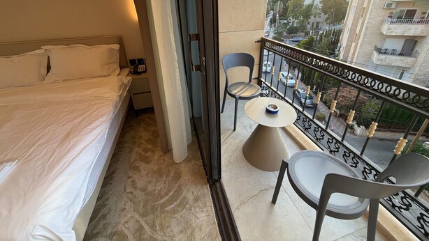 Habitación de hotel con cama, escritorio con teléfono, silla, mesita y balcón con vista a la ciudad.