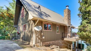 A two-story house with a stone chimney, satellite dish, and a balcony overlooking a body of water. - Decked Out! Private Dock Escape on Watts Bar Lake (Spring City)
